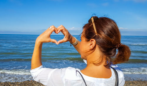 Rear view of young woman standing in sea against sky