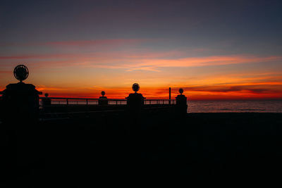 Silhouette people on beach against orange sky