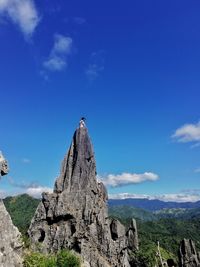 Low angle view of woman on rock formation against blue sky