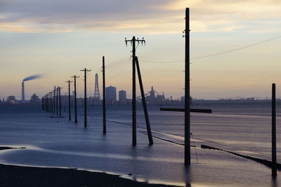 Wooden posts in sea against sky during sunset