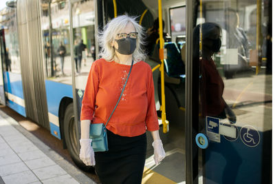 Woman wearing face mask standing near bus