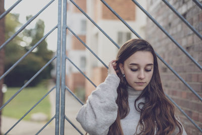 Young woman looking down while standing against metal gate