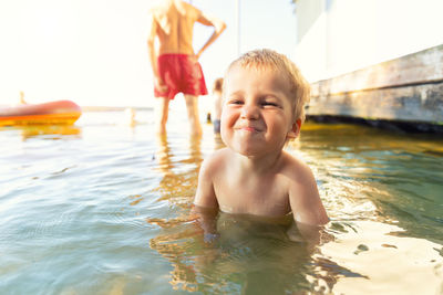 Portrait of smiling shirtless boy sitting in lake