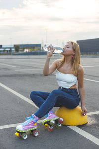 Young woman drinking water while sitting on road in city