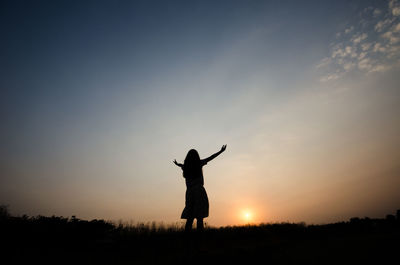 Silhouette woman with arms outstretched standing on land against sky during sunset