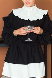Cropped picture of fashion woman in vintage black and white dress holding elegant glass for cocktail