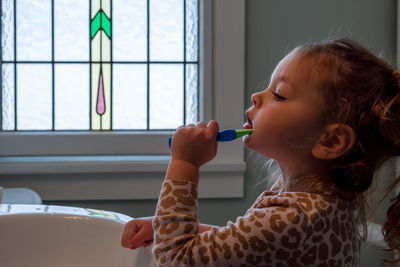 Side view of girl brushing teeth at home