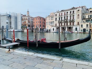 Boats moored in canal by buildings in city against sky