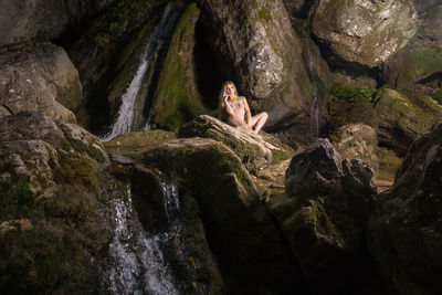 Woman sitting on rock against waterfall