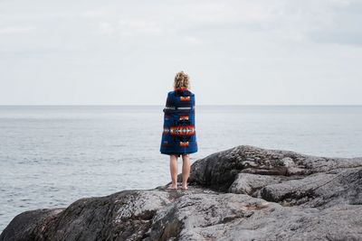 Woman standing on rocks wrapped in a pendleton blanket in sweden