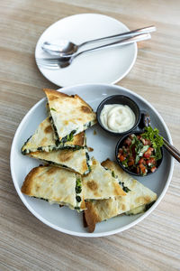 Quesadilla in a round plate, next to an empty plate and cutlery, on a wood table, natural light. 