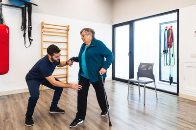 Male instructor supporting old woman using train in gym