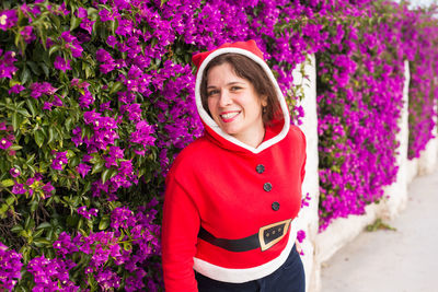 Portrait of smiling young woman standing by pink flowering plants