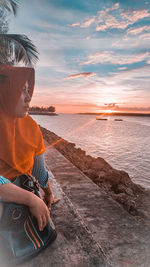 Man sitting on beach against sky during sunset