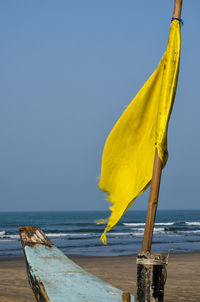 Close-up of yellow flag on beach against clear sky