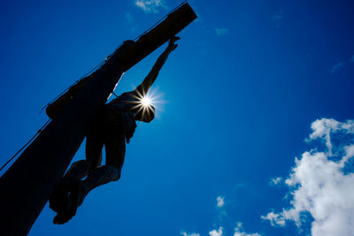 Low angle view of silhouette sculpture against blue sky on sunny day