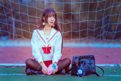 Young woman listening to music while sitting against net on soccer field