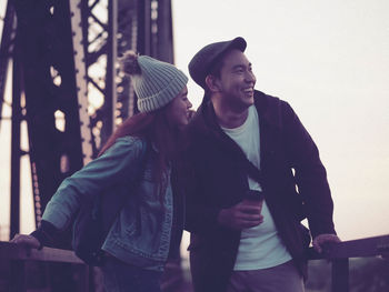 Cheerful young couple standing against clear sky at sunset