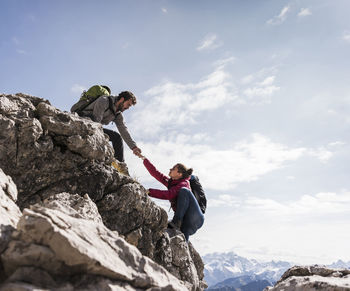 Germany, bavaria, oberstdorf, man helping woman climbing up rock