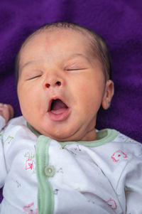 Newborn baby isolated yawning in white cloth with purple background from different angle