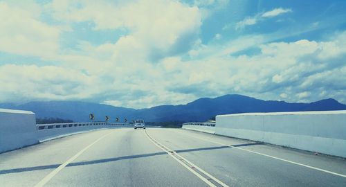 Road passing through mountains against cloudy sky