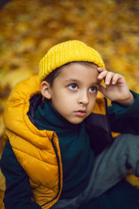 Portrait of a fashionable child boy autumn sitting on a trail in orange leaves in the afternoon