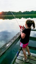 Full length of girl fishing on lake against sky