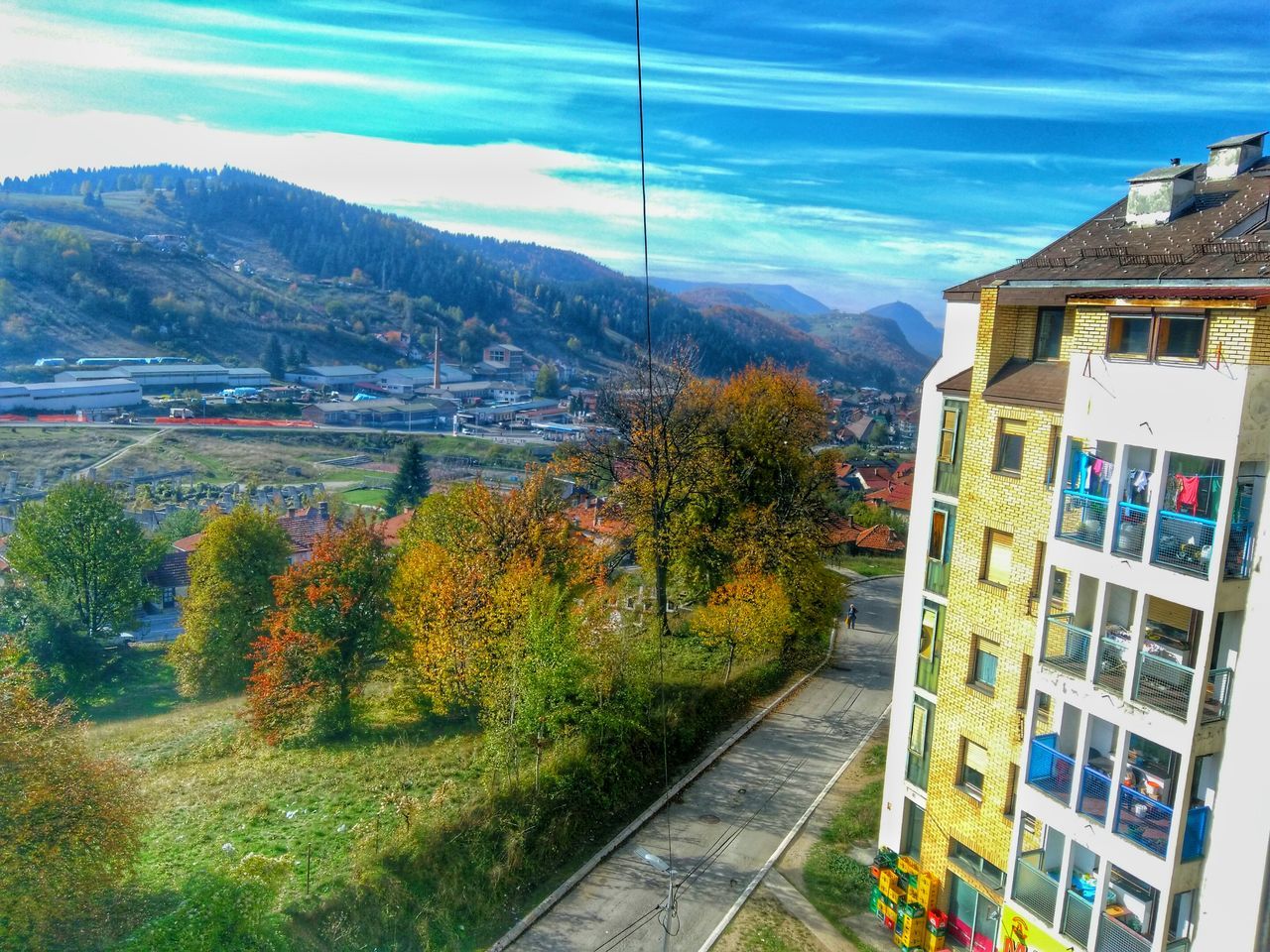 mountain, built structure, building exterior, sky, architecture, transportation, tree, house, day, power line, mountain range, nature, residential structure, blue, outdoors, landscape, village, town, mode of transport, cloud