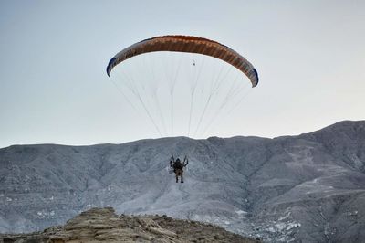 Person paragliding over mountains against sky