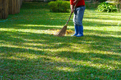 Low section of person with broom standing on grassy land in yard