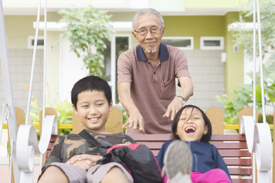 Happy siblings with grandfather swinging in playground