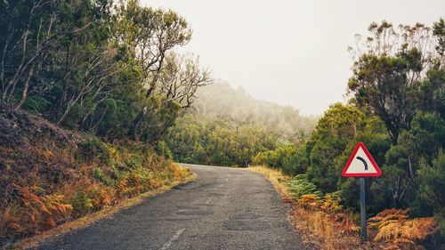 Road sign by trees against sky