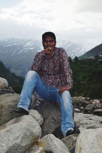 Full length of man sitting on rock against mountains