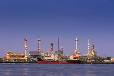 View of factory by sea against clear blue sky