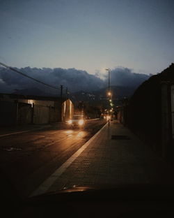 Illuminated street against sky at night