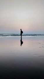 Silhouette man standing at beach against clear sky during sunset