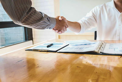 Close-up of business colleagues shaking hands at desk in office
