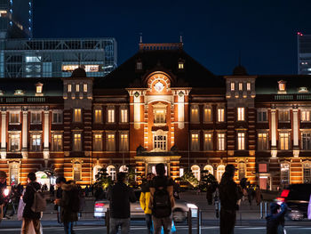 People on street against illuminated buildings in city at night