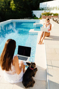 Women sitting by swimming pool against trees