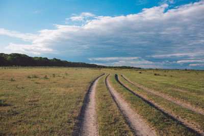 Dirt road amidst field against sky