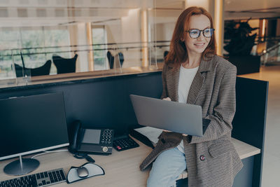 Portrait of young woman using digital tablet while standing in office