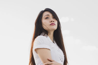 Thoughtful young woman standing against white background