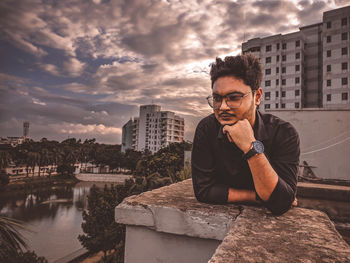 Young man sitting in city against sky