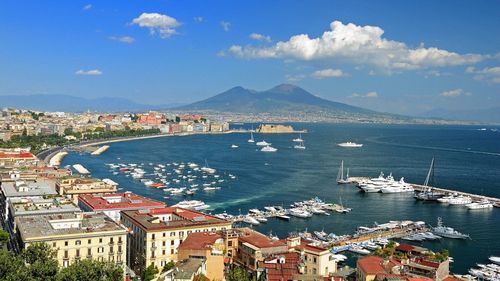 High angle view of cityscape by sea against blue cloudy sky