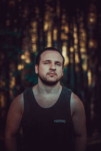 Portrait of young man standing against trees in forest