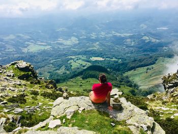 Rear view of man sitting on rock looking at mountains