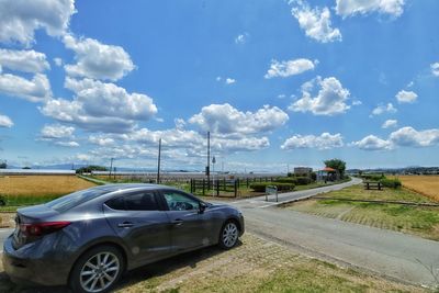 Car on road by field against sky