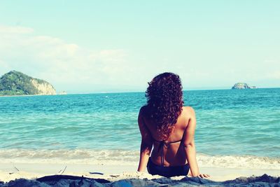 Rear view of young woman relaxing on shore at beach