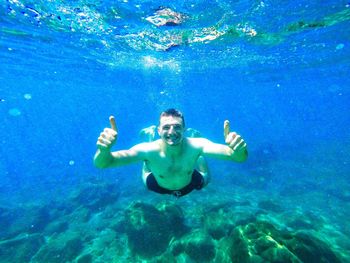 Portrait of shirtless young man gesturing thumbs up in sea