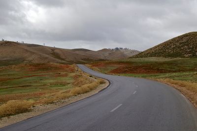 Country road leading towards mountains against sky